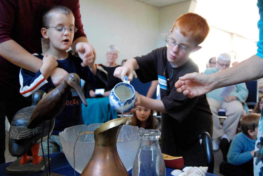 adults help two young boys pour water into a bowl