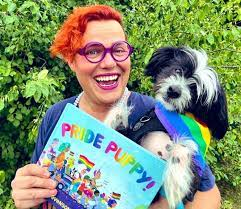 Gender Diverse Person with dog holding a book called "Pride Puppy"